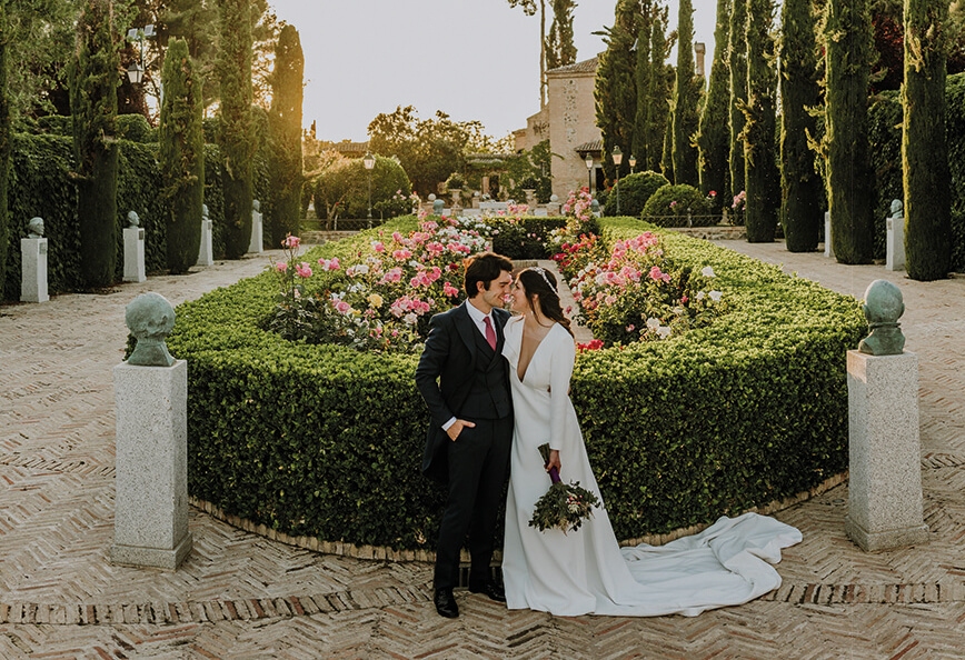 Pareja de novios enamorados mirándose tiernamente en el patio de rosales del Cigarral del Ángel de Toledo