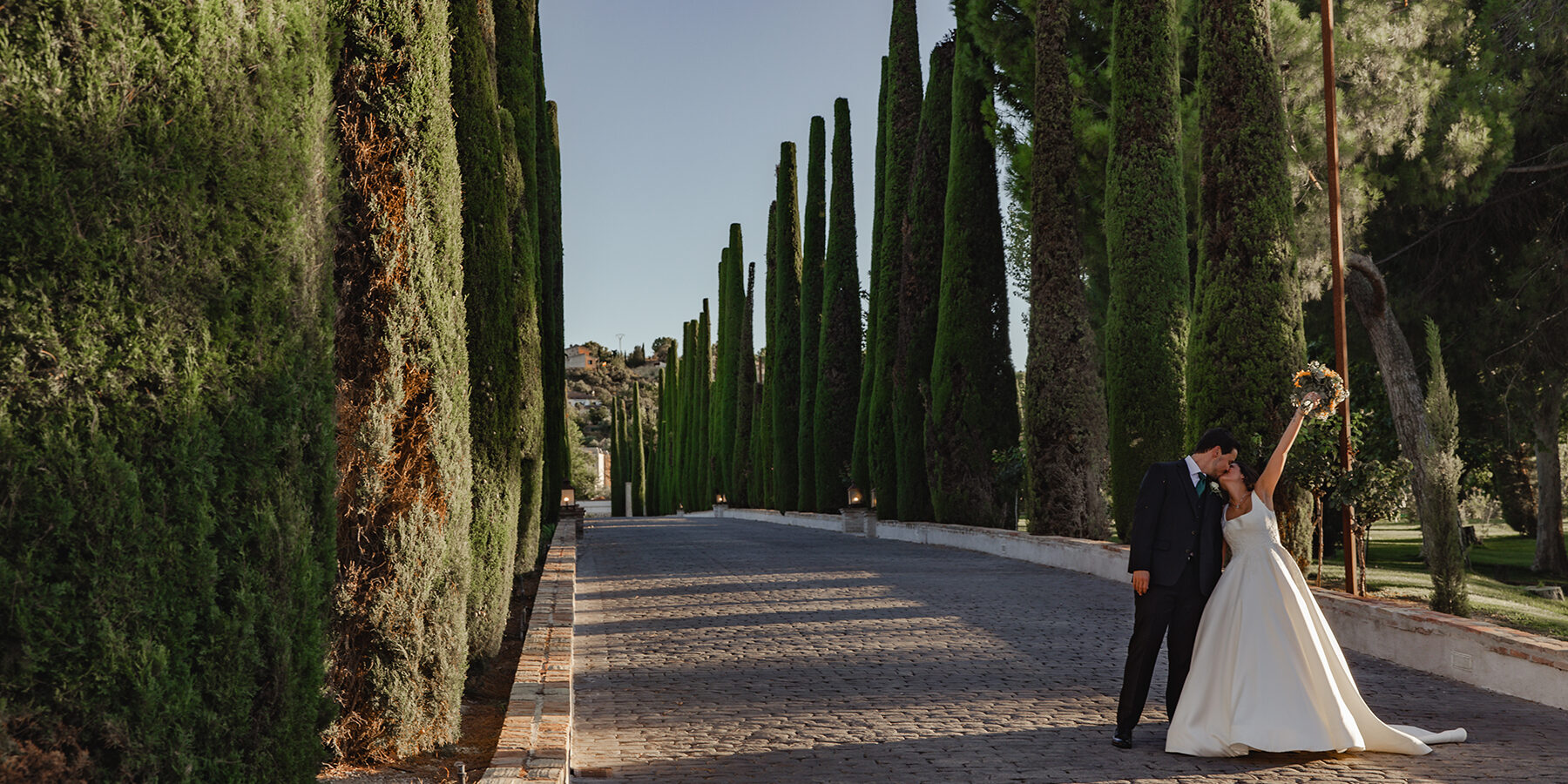 novios-besandose.jpg Pareja de novios besándose con la novia levantando el ramo de flores en el Paseo de Cipreses del Cigarral del ángel de Toledo