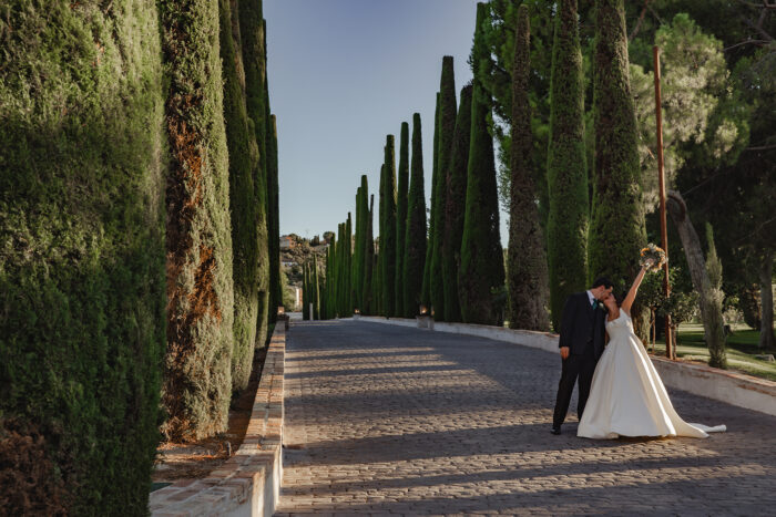 Pareja de novios besándose con la novia levantando el ramo de flores en el Paseo de Cipreses del Cigarral del ángel de Toledo